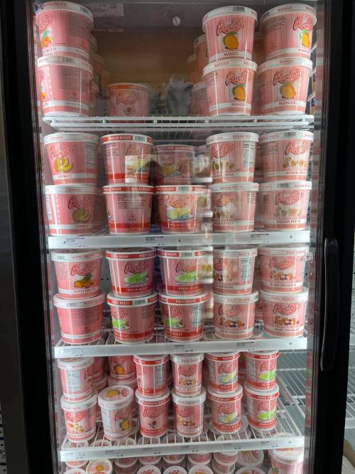 A freezer filled with various flavors of ice cream tubs, all in pink packaging, neatly arranged on shelves.