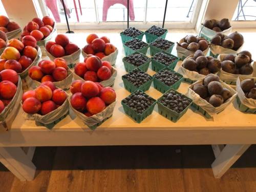 A table displaying baskets of red apples, blueberries, and dark pears in a bright, sunny setting.