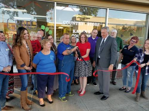 A group of people gathers for a ribbon-cutting ceremony at a country store, smiling and celebrating the opening.