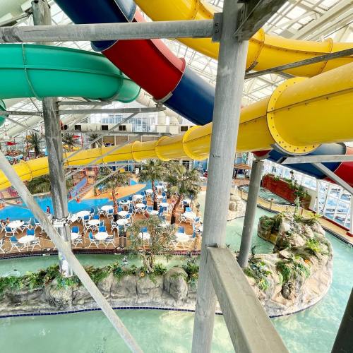 A vibrant indoor water park featuring colorful water slides, a pool, and lounge chairs surrounded by tropical plants.