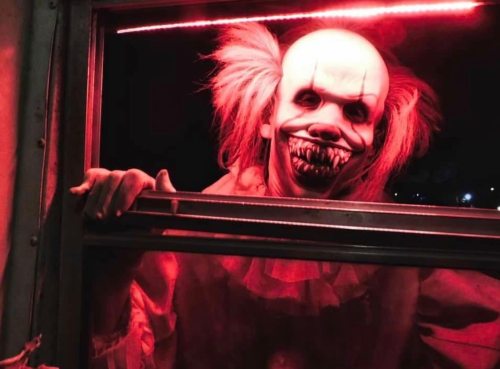 A creepy clown with a sinister grin peers through a window, illuminated by red light.