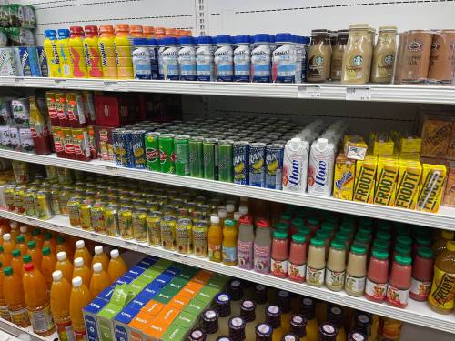A grocery store shelf filled with various beverages, including sodas, juices, and dairy drinks in colorful packaging.