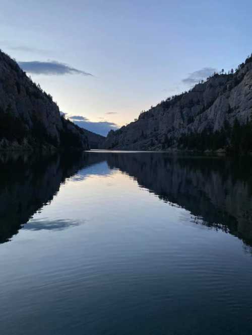 A serene lake surrounded by mountains at dusk, reflecting the sky and landscape in calm waters.