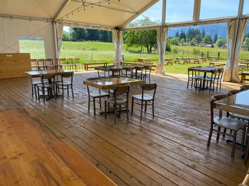 A spacious tent with wooden floors, empty tables, and chairs, surrounded by greenery and mountains in the background.