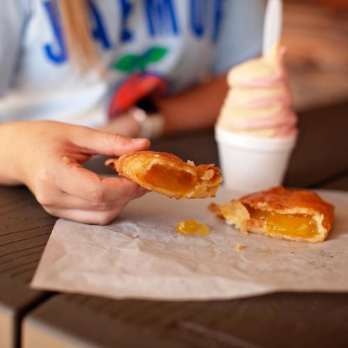 A hand holding a pastry with a bite taken out, next to a cup of soft serve ice cream on a table.