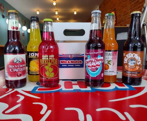 A variety of colorful soda bottles arranged around a "Mix & Match" box on a table.