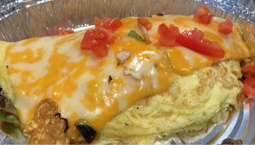 A cheesy omelette topped with diced tomatoes, served in a silver takeout container.