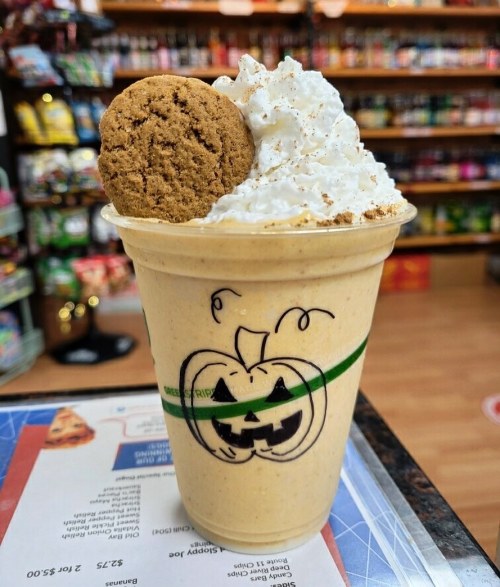 A festive pumpkin-flavored drink topped with whipped cream and a cookie, decorated with a playful pumpkin drawing.
