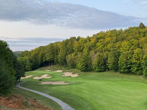 A scenic view of a golf course surrounded by trees, featuring sand traps and a winding path.