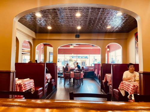 Interior of a restaurant featuring red-checkered tablecloths, booths, and diners enjoying their meals.
