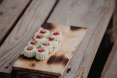 A wooden board with decorative sushi rolls topped with pink accents, placed on a rustic wooden surface.