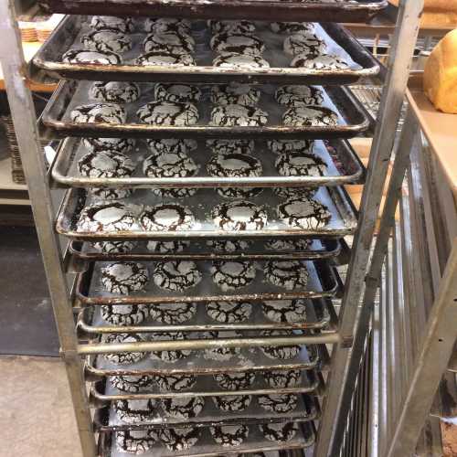 A metal rack filled with trays of freshly baked chocolate crinkle cookies, dusted with powdered sugar.