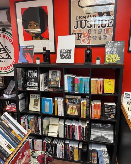 A bookshelf filled with books on Black history and culture, featuring artwork and decorative items on a vibrant red wall.