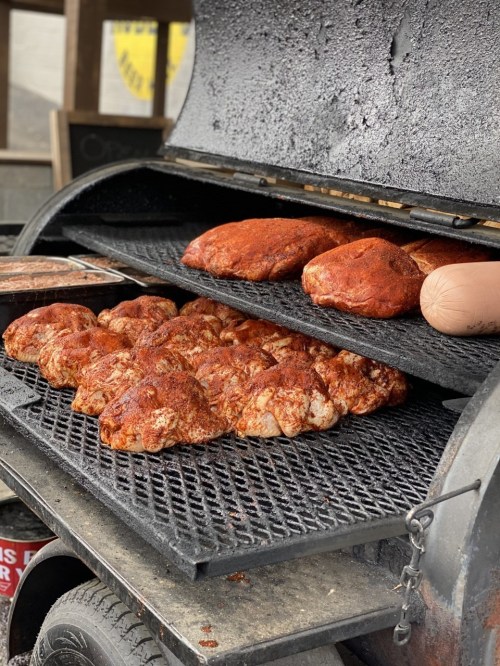 Smoked meats on a grill, featuring several seasoned pork shoulders on the top and bottom racks.