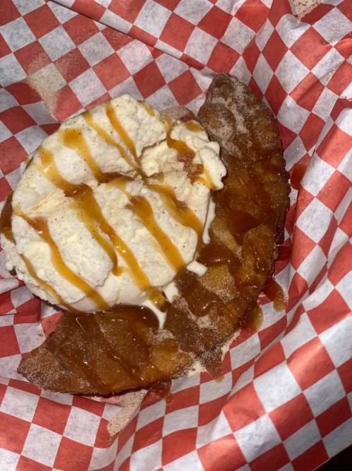 A dessert featuring a fried pastry topped with ice cream and drizzled with caramel sauce, served in a red-checkered basket.