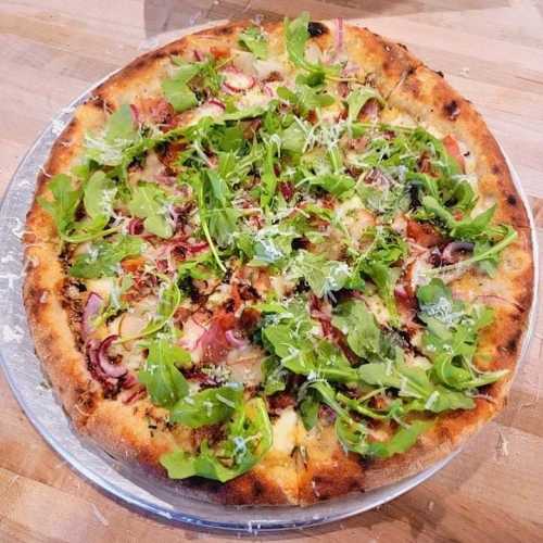 A freshly baked pizza topped with arugula, cheese, and various vegetables on a silver serving tray.