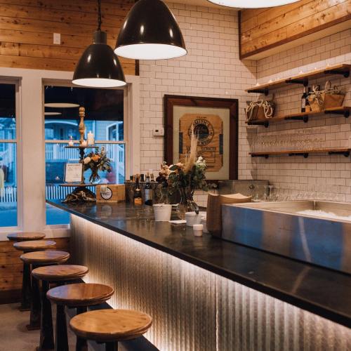 A cozy café interior featuring a wooden bar, stools, and warm lighting, with shelves and decorative items on the wall.