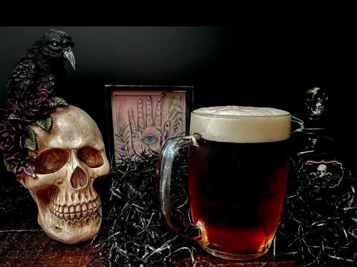 A dark-themed scene featuring a skull with roses, a crow, and a frothy mug of beer on a wooden surface.
