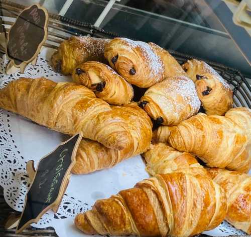 A display of various pastries, including croissants and chocolate-filled rolls, on a lace doily in a bakery.