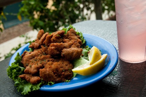 A blue plate of golden-brown fried food on lettuce, garnished with lemon wedges, next to a glass of pink drink.