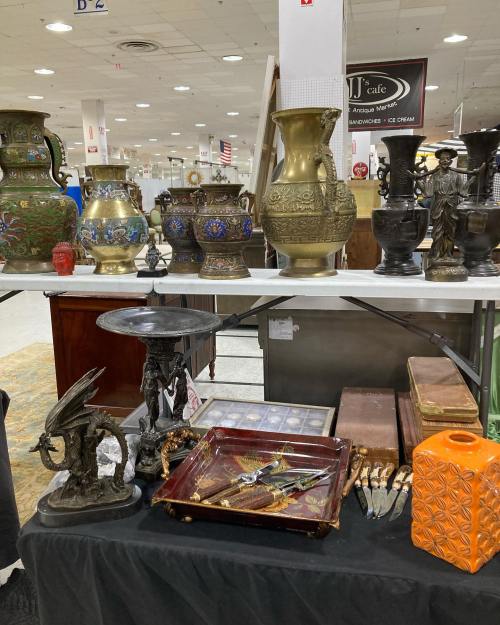 A display of various antique vases, sculptures, and decorative items on a table in a market setting.
