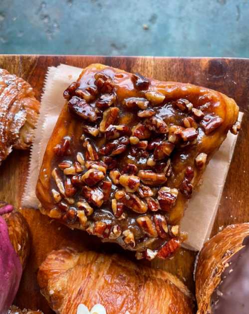 A close-up of a caramel pecan pastry topped with chopped pecans on a wooden board.