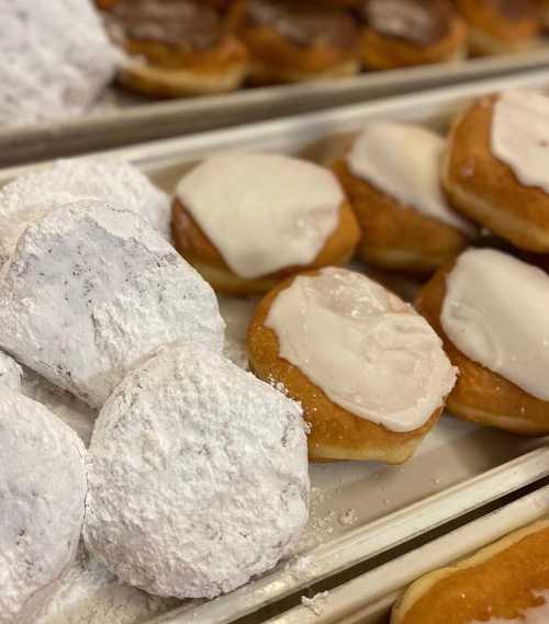 A close-up of assorted donuts, including powdered and frosted varieties, arranged on a tray.