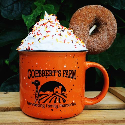 An orange mug with whipped cream and sprinkles, next to a donut, set against a green background.
