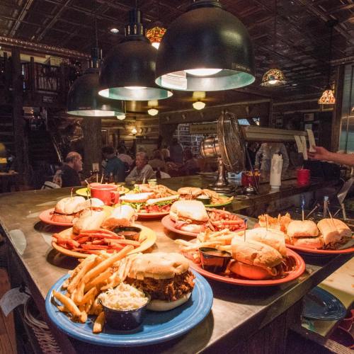 A vibrant restaurant scene featuring a variety of burgers, fries, and sides on colorful plates under hanging lights.