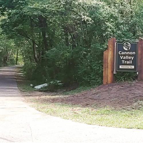 Sign for Cannon Valley Trail, surrounded by greenery, with a path leading into the woods.