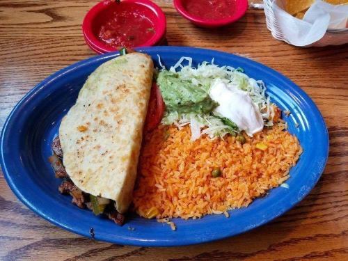 A blue plate with a taco, rice, lettuce, guacamole, and sour cream, accompanied by red salsa on the side.