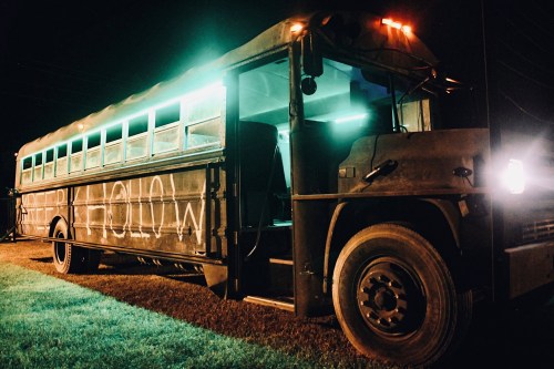 A dark school bus with "SLEEPY HOLLOW" painted on the side, illuminated by green lights at night.