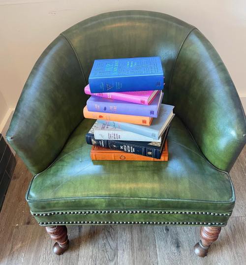 A green armchair with a stack of colorful books resting on its seat.