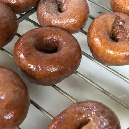 Freshly glazed donuts cooling on a wire rack, showcasing a golden-brown color and shiny glaze.