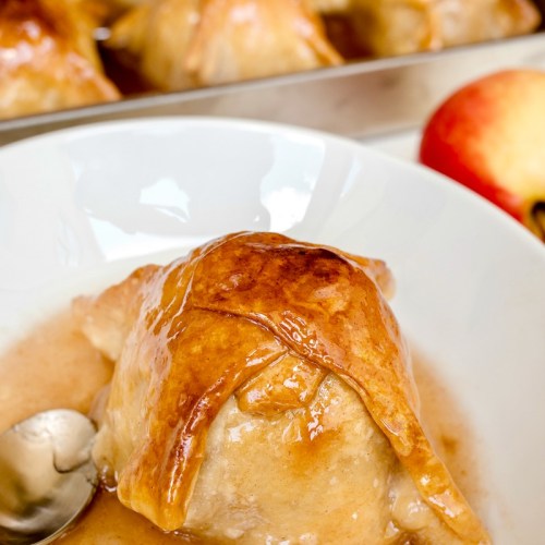 A close-up of a golden-brown baked dessert with a spoon, served in a bowl with a sweet sauce.
