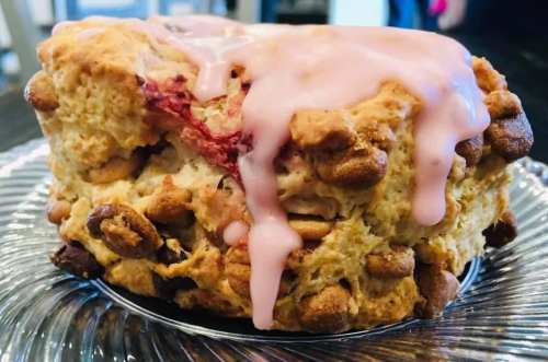 A close-up of a baked good topped with pink icing, featuring a crumbly texture and bits of cereal on the sides.