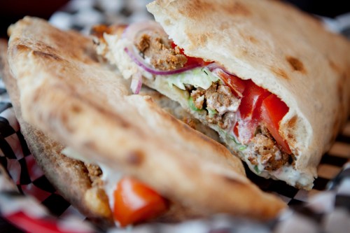 A close-up of a pita sandwich filled with chicken, tomatoes, lettuce, and onions, served on a checkered plate.