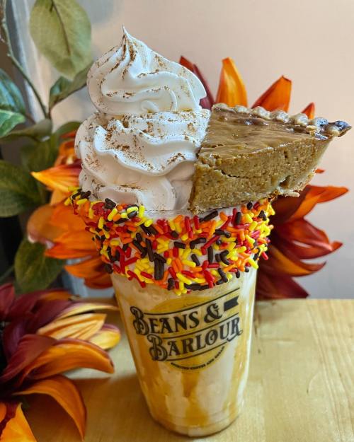 A decadent milkshake topped with whipped cream, pie slice, and colorful sprinkles, surrounded by autumn flowers.