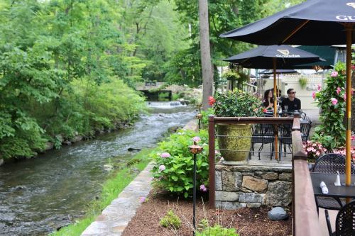 A scenic riverside patio with tables, umbrellas, and lush greenery along a flowing stream.