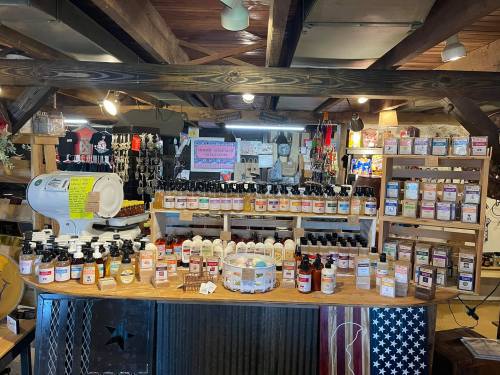 A rustic shop display featuring various bottles and jars of products on wooden shelves, with merchandise in the background.