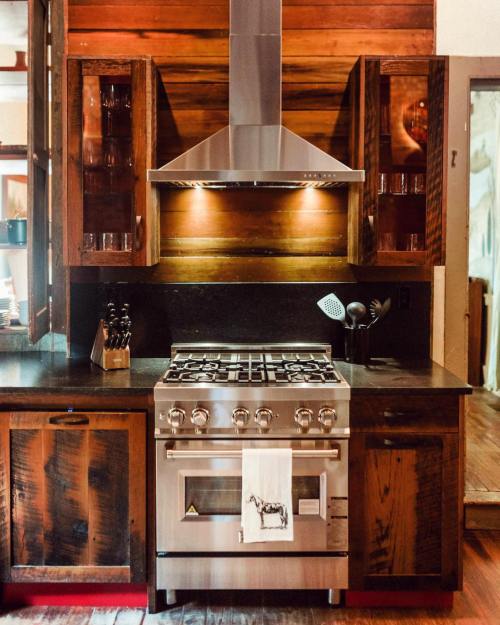 Modern kitchen with wooden cabinets, a stainless steel stove, and a sleek hood above, featuring warm lighting.