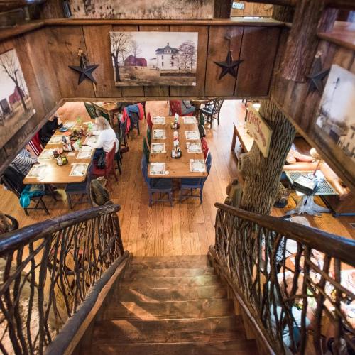 A rustic dining area with wooden decor, tables set for meals, and a staircase leading down to the space.
