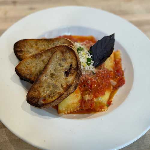 A plate of pasta with tomato sauce, topped with cheese and fresh basil, accompanied by toasted bread slices.