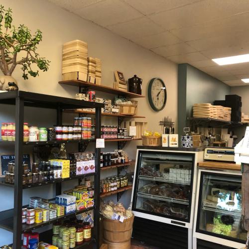 A cozy shop interior with shelves of jars, canned goods, and a display case, featuring a clock and wooden storage boxes.