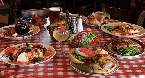 A table set with various dishes, including seafood, salads, and drinks, all on a checkered tablecloth.