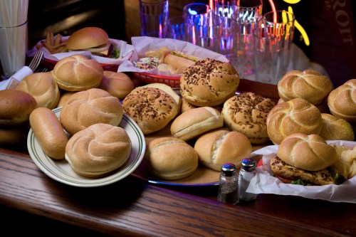 A variety of hamburger buns and rolls displayed on a wooden table, with colorful neon lights in the background.