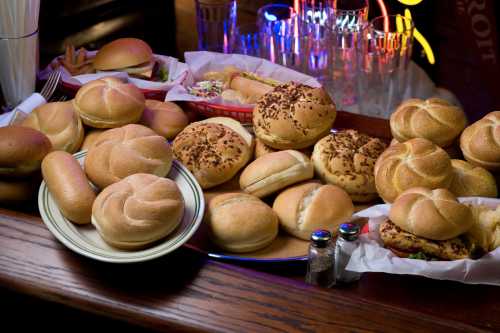 A variety of hamburger buns and rolls displayed on a wooden table, with colorful neon lights in the background.