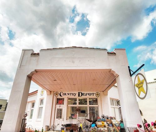 A charming storefront of "Country Depot" with decorative items and a blue sky filled with clouds above.