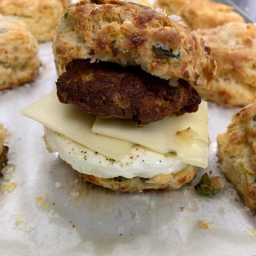 A biscuit sandwich with a sausage patty, cheese slice, and a fried egg, served on a baking sheet.