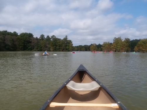 A view from the front of a canoe on a calm lake, with other kayakers in the distance and trees lining the shore.